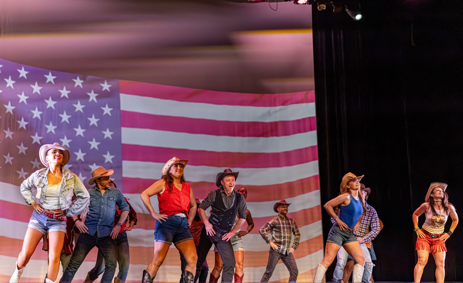 The full 2026 cast performing the opening ensemble number in front of a large flag backdrop.