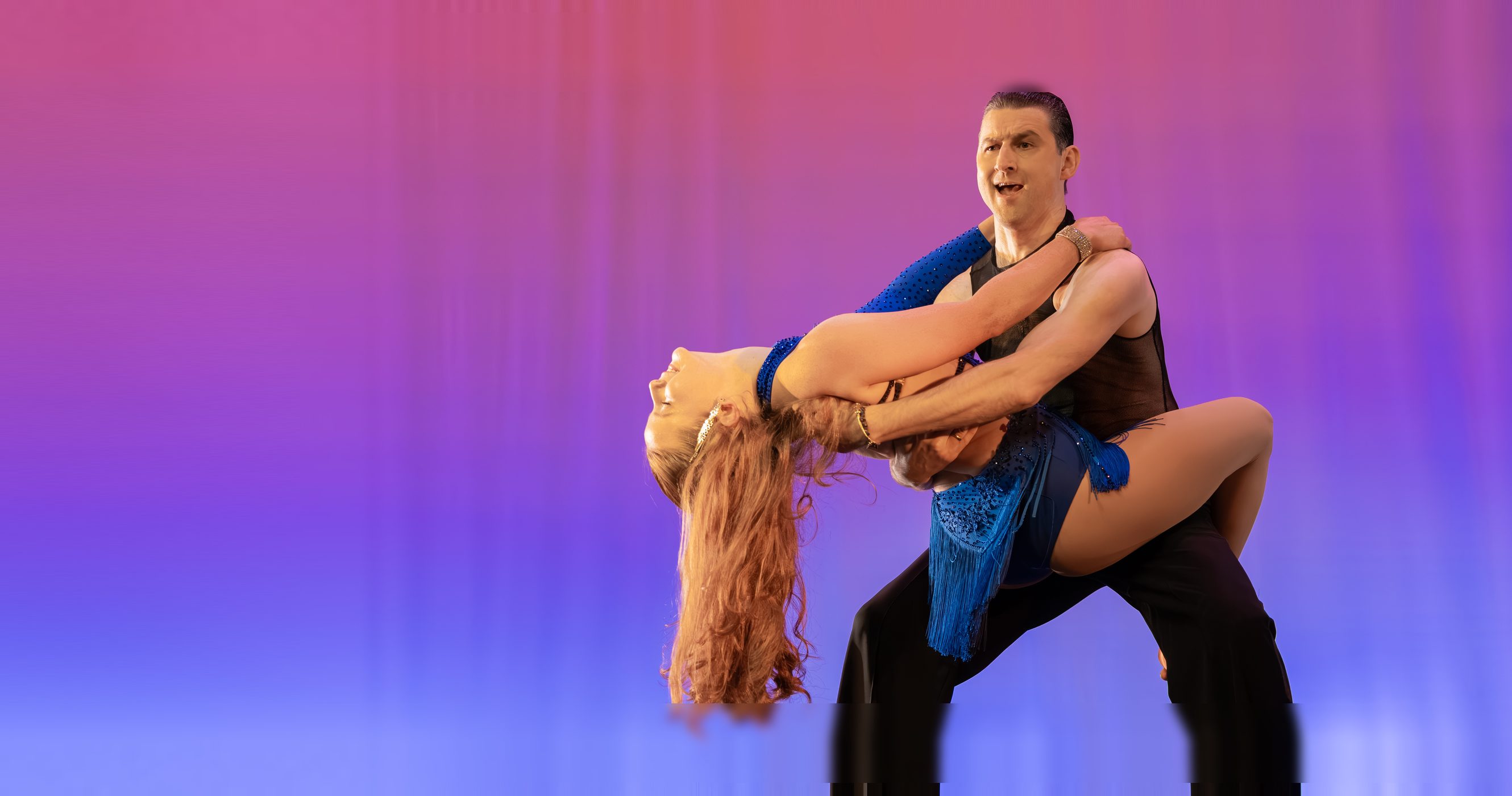 A community dancer in a blue fringe dress lifted by her Arthur Murray partner on the Lewis Auditorium stage at Dancing Stars of St. Johns County.