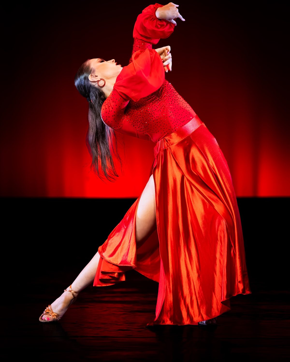 A community dancer in a red fringe dress finishing a routine with her professional partner under stage lights.