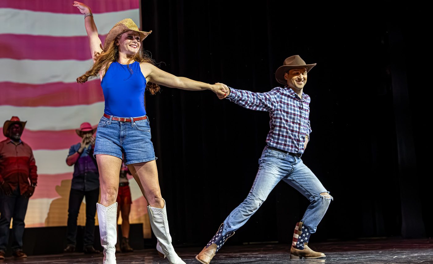A community dancer and her professional partner mid-routine in front of the flag backdrop.